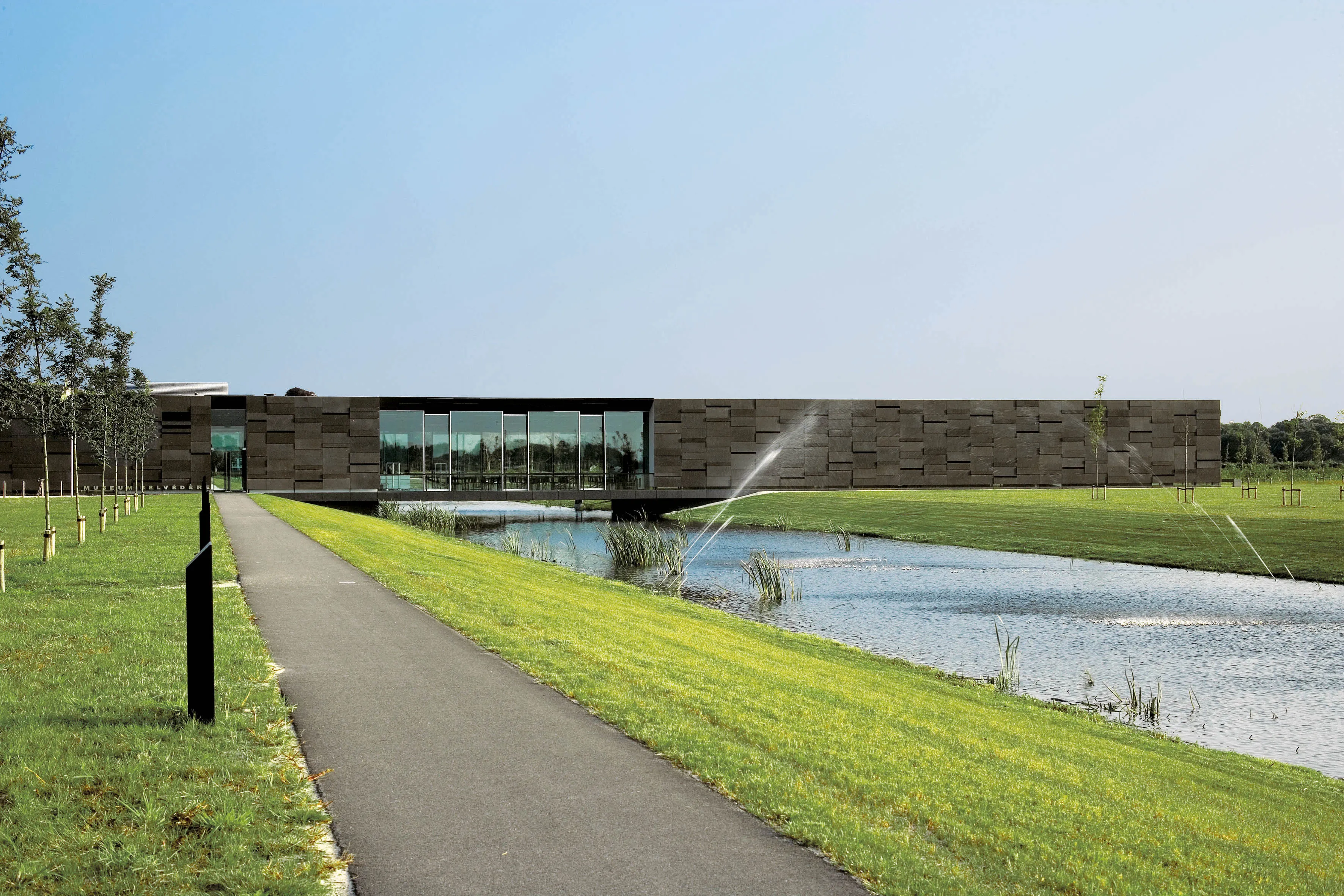 Het langgerekte moderne gebouw van Museum Belvedère in Heerenveen, aan het water met een wandelpad ernaartoe